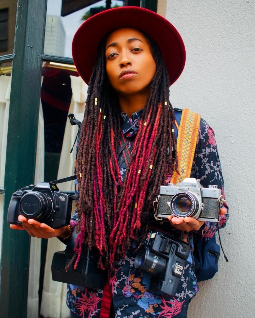 Shakita Alford of Ki Shot It Visuals wearing a red hat and holding cameras